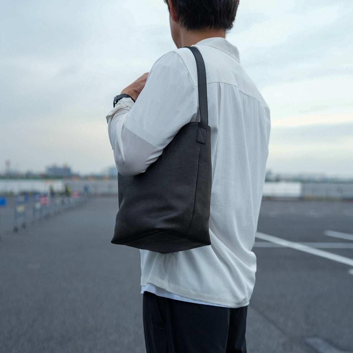 レザーバケットバッグを持ったメンズの日常スタイル シンプルで洗練されたミニショルダーバッグ
